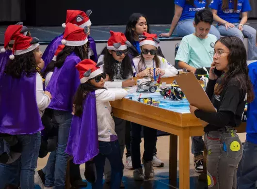 Niñas con gorro navideño y lentes participan en el juego del robot de FIRST LEGO League en PrepaTec Laguna