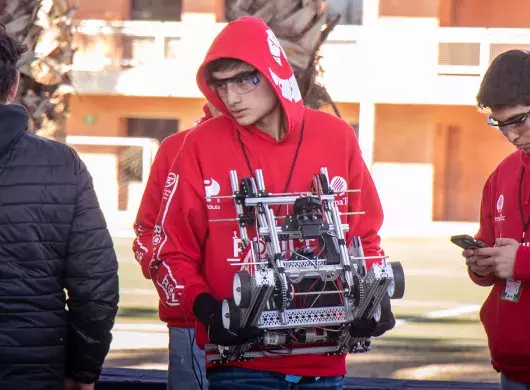 Estudiante joven lleva robot en sus manos en su participación en competencia de robótica