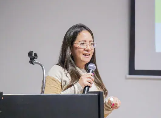 Directora del programa de Licenciatura en Contaduría Pública y Finanzas sostiene micrófono durante conferencia