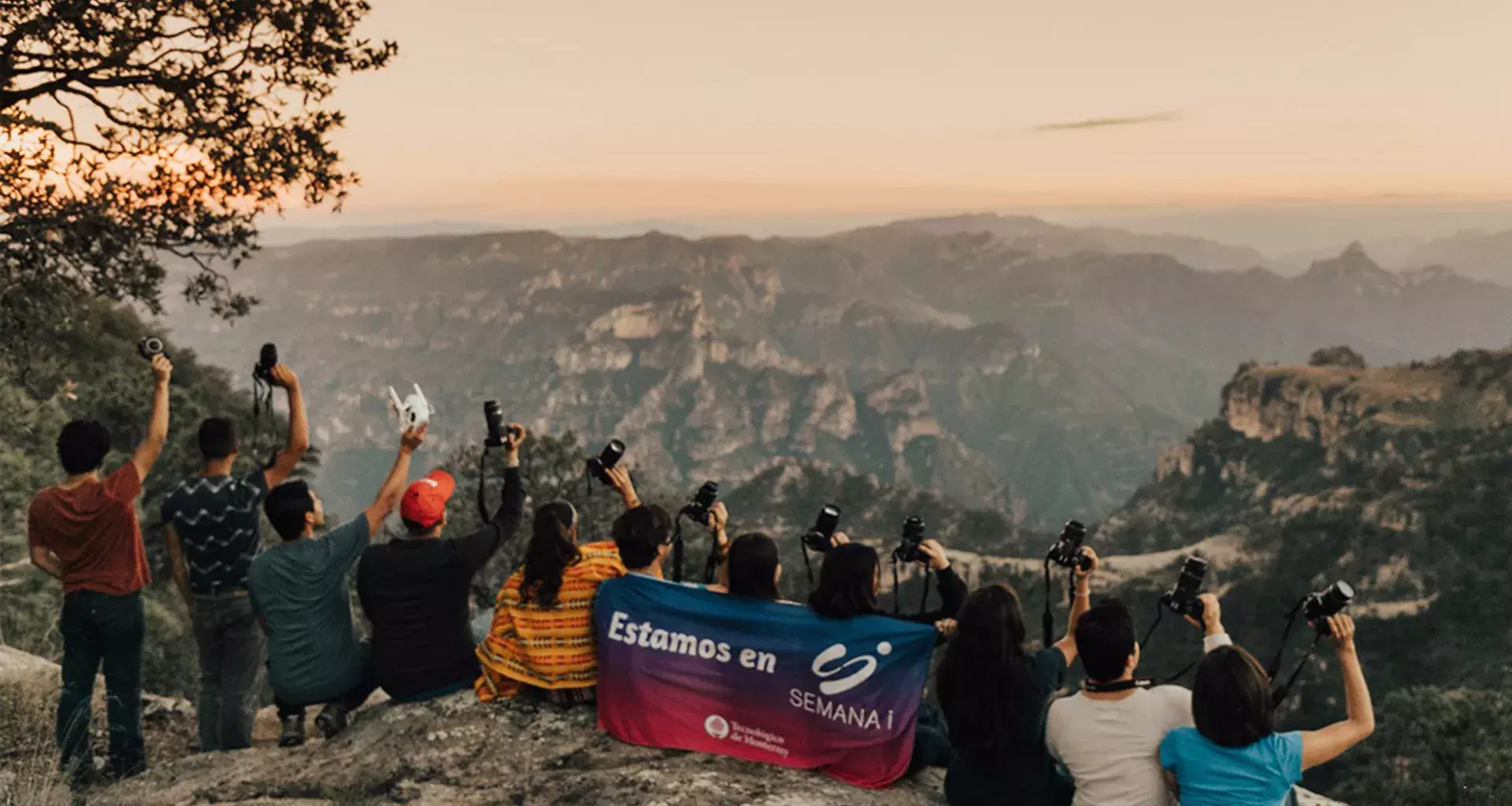 Jovenes sostienendo cámaras fotográficas sentados en un acantilado