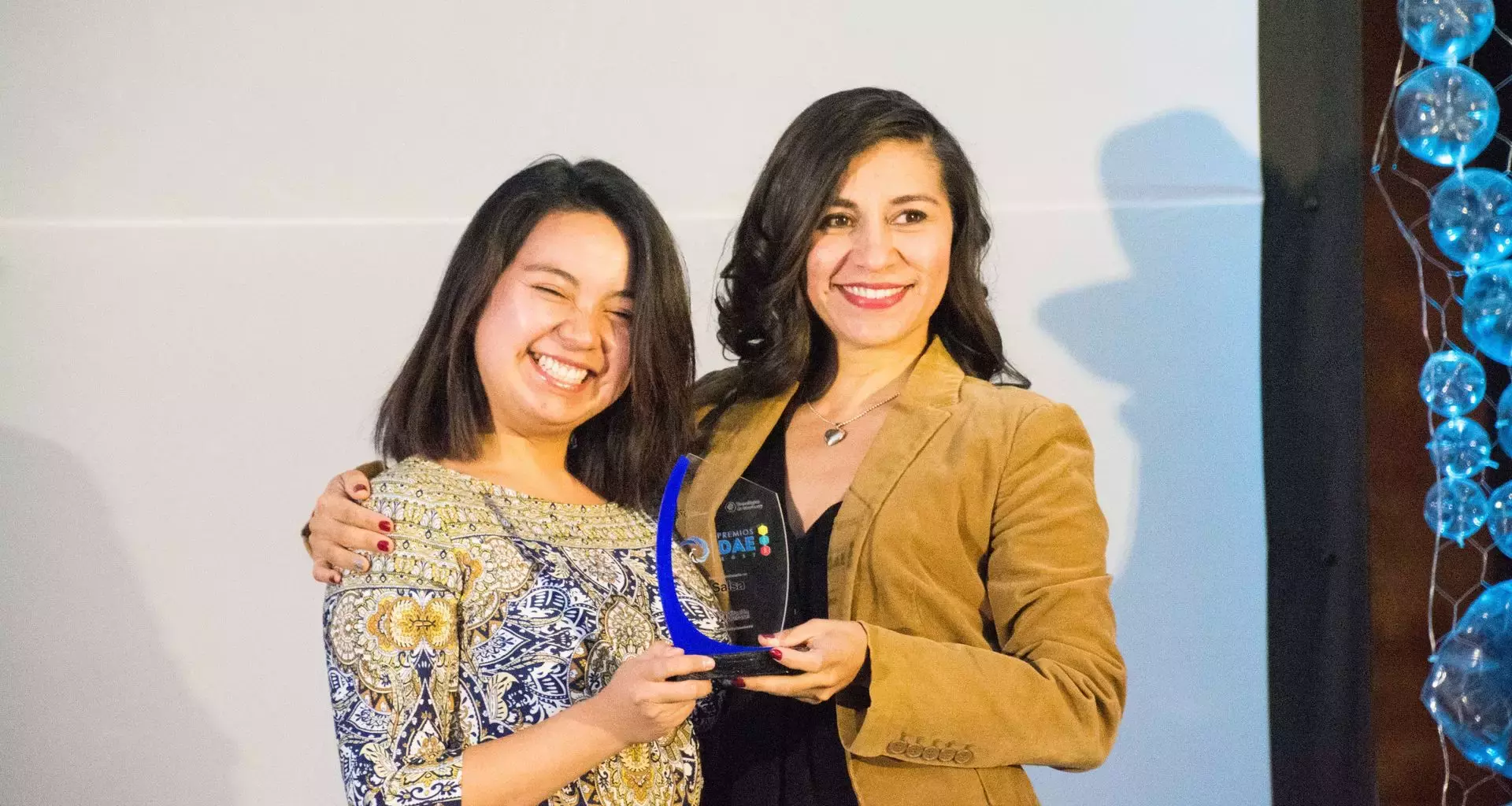 Maestra abrazando a su alumno sosteniendo un premio