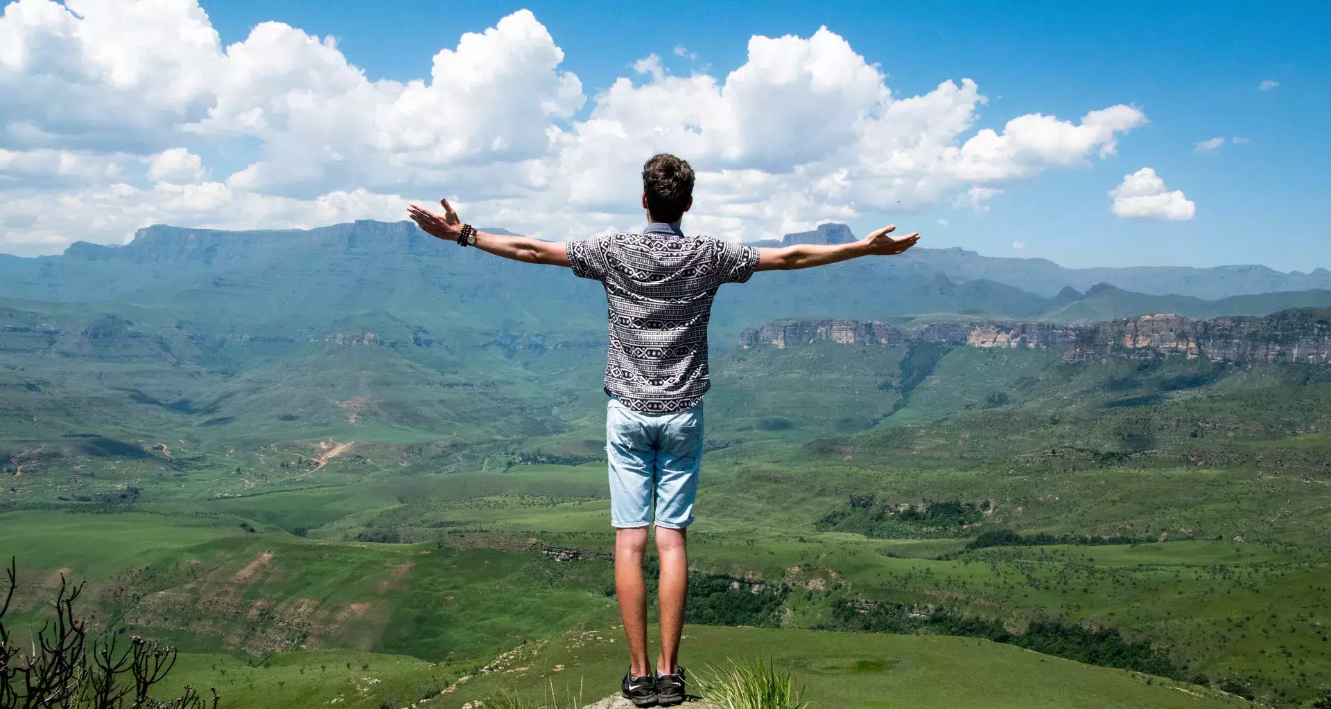 Joven de espalda en la cima con los brazos abiertos y con la mirada al horizonte