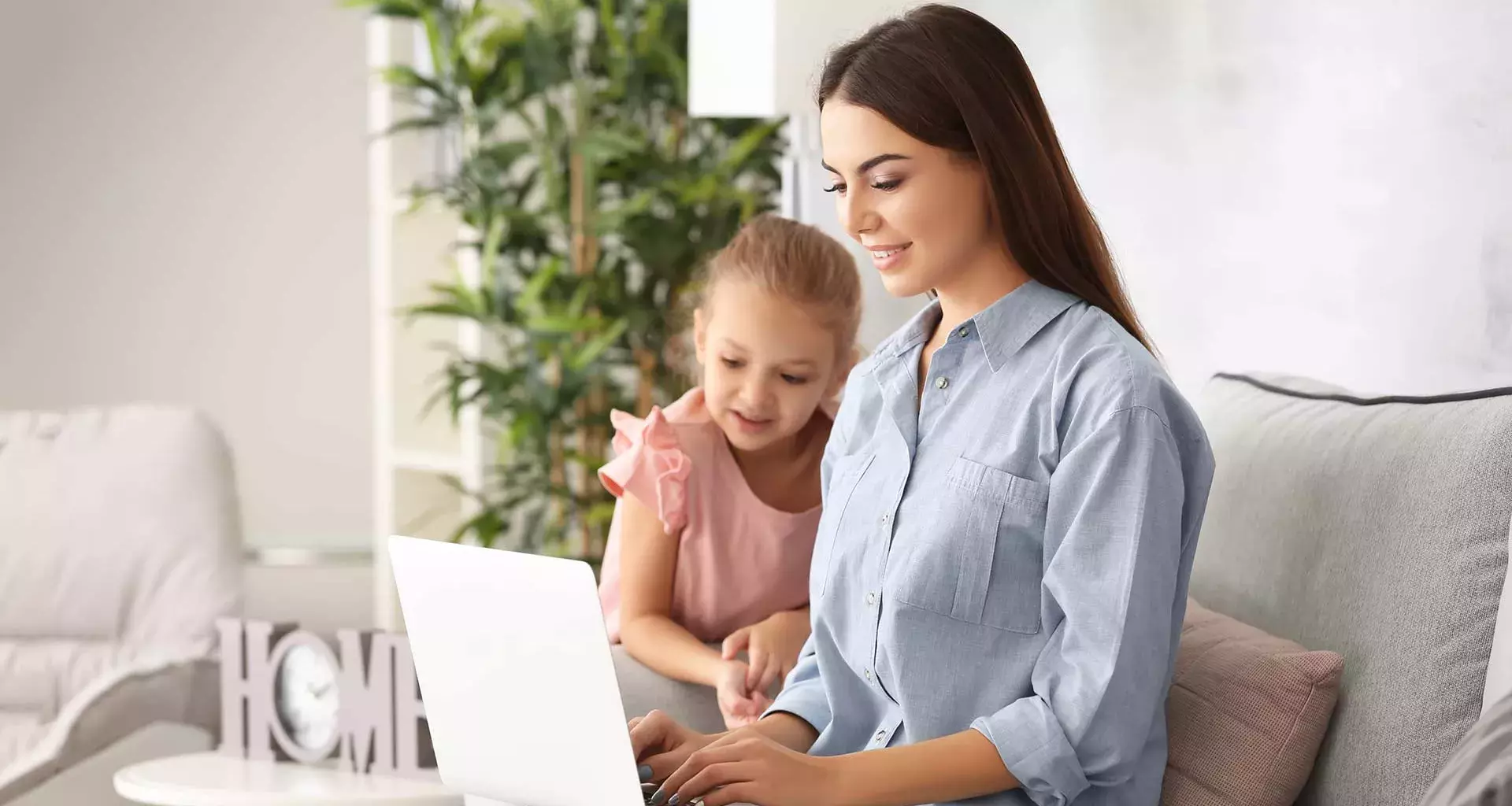 Madre de familia trabajando en su laptop, con su hija a una lado