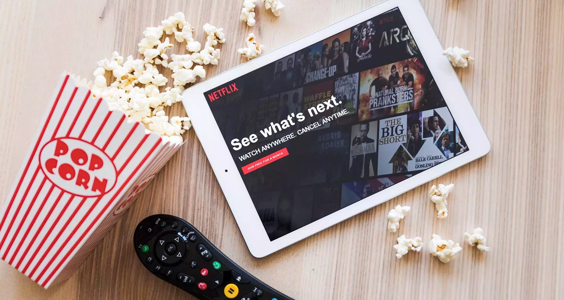 Ipad con Netflix en pantalla a un lado de palomitas y control remoto 