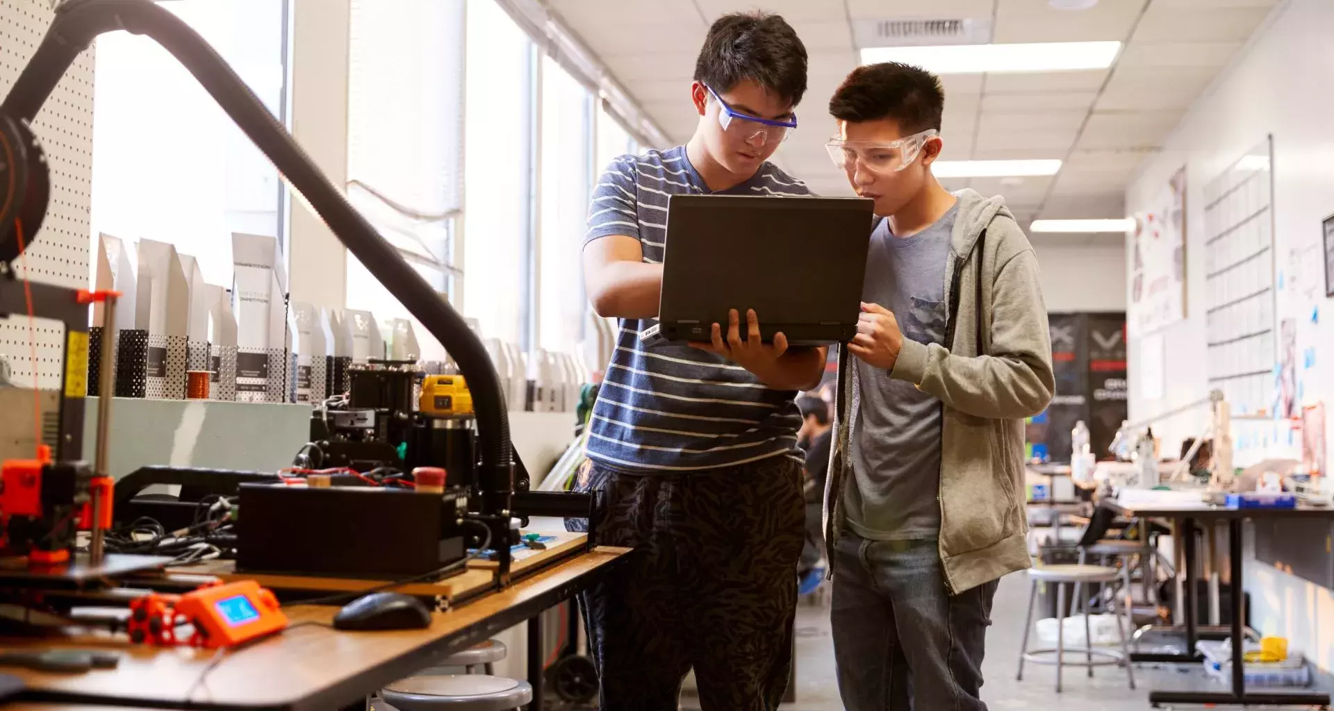 2 jóvenes estudiantes en un laboratorio; uno de ellos sostiene una laptop en su mano y señala su pantalla