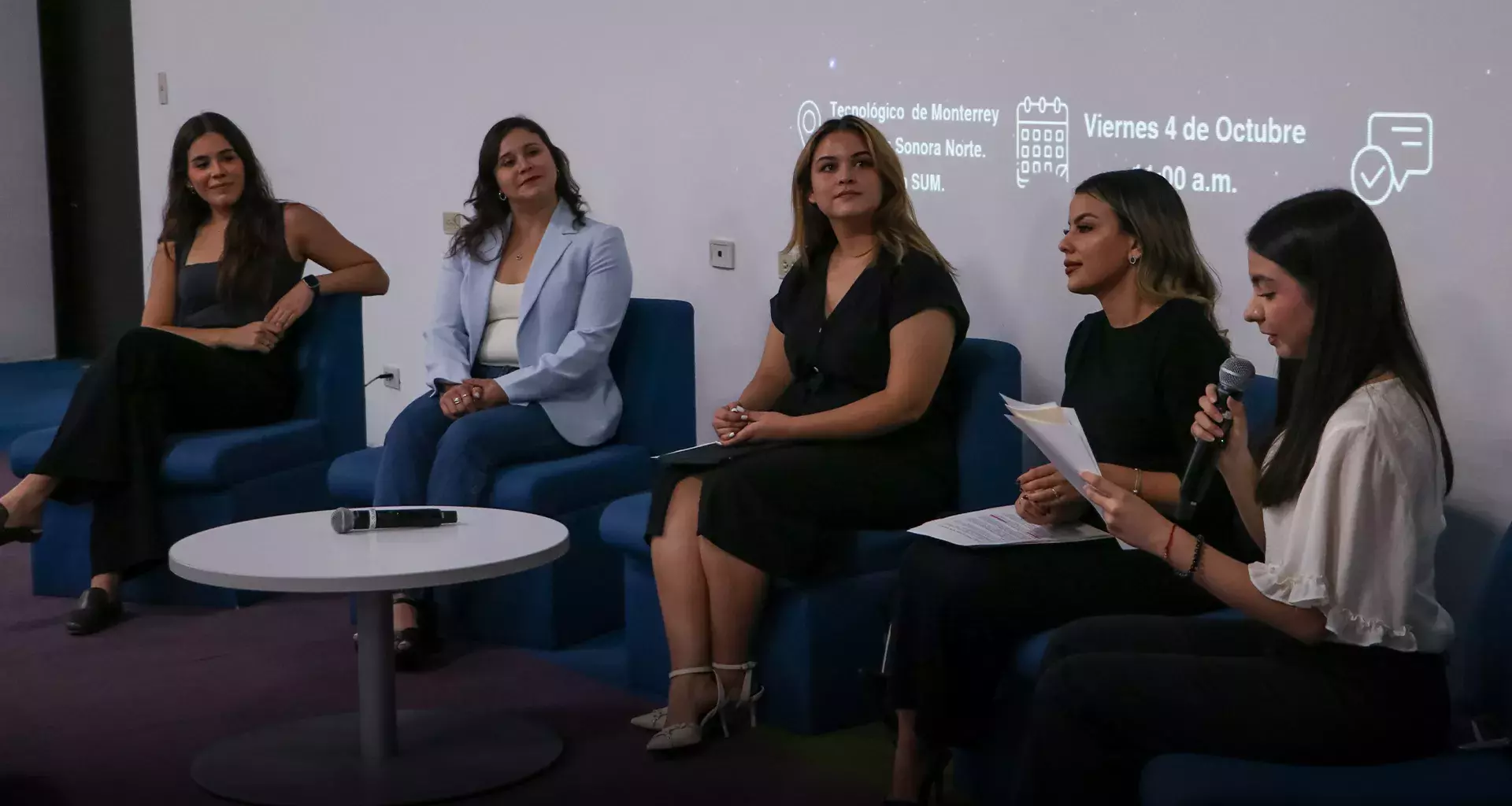 5 mujeres sentadas en sillones azules platicando