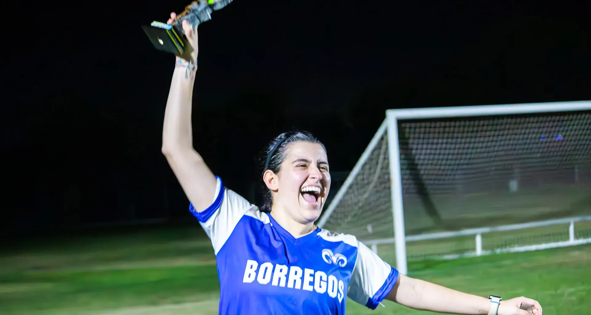 Jugadora de Borregos Laguna con uniforme azul y blanco festeja con el trofeo de primer lugar el campeonato femenil de fútbol soccer