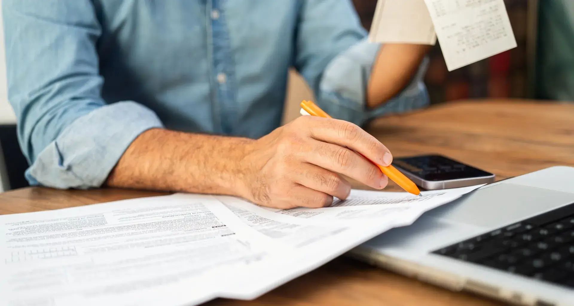 Hombre en camisa de mezclilla calculando impuestos con Comprobante y formas en un escritorio de madera. Concepto de preparación de impuestos y gestión financiera