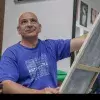 Profesor de artes plásticas pintando un cuadro con ligera sonrisa volteando hacia arriba.