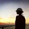 Ashly Hinojos con casco y uniforme naranja mirando el atardecer sobre el mar desde una plataforma petrolera.