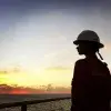 Ashly Hinojos con casco y uniforme naranja mirando el atardecer sobre el mar desde una plataforma petrolera.