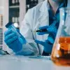 Científicos en un laboratorio de biotecnología analizando muestras líquidas y tubos de ensayo enfocados en la prevención de bacterias hospitalarias.