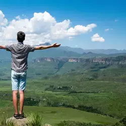 Joven de espalda en la cima con los brazos abiertos y con la mirada al horizonte