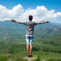 Joven de espalda en la cima con los brazos abiertos y con la mirada al horizonte