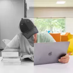 Joven observando un libro y una computadora