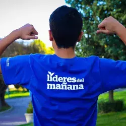 Chico de espaldas señalando la playera que dice: Líderes del Mañana