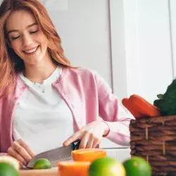 Mujer joven en una cocina cortado un limón con frutas y verduras