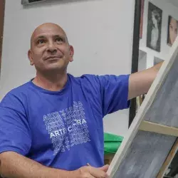 Profesor de artes plásticas pintando un cuadro con ligera sonrisa volteando hacia arriba.