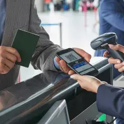 Representante de atención al cliente escaneando el código QR del pase de abordar en un teléfono inteligente en el mostrador de check-in del aeropuerto.