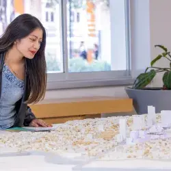 Jana, estudiante del Tec, observa una maqueta urbana sobre una mesa dentro de un salón iluminado, analizando con atención el modelo arquitectónico frente a ella.