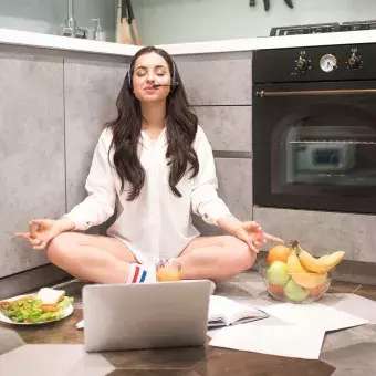 Joven con computadora, en posición de yoga y comida saludable alrededor, para representar el concepto de una rutina equilibrada