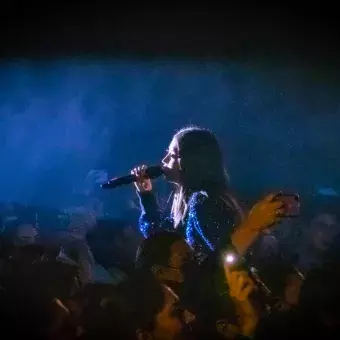 Alumna cantando con luz en cara en medio de la audiencia