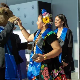 TEUS, la mascota del Tec, saludando a una egresada del campus Puebla con vestimenta típica del estado