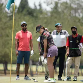 Grupo de golfistas viendo a una jugadora intentar un putt