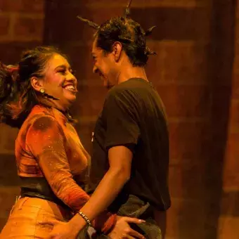 Alumnos sonríen mirándose mutuamente mientras interpretan escena de amor en la obra 