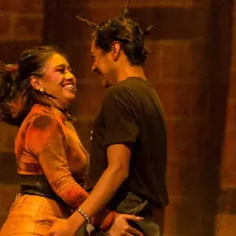 Alumnos sonríen mirándose mutuamente mientras interpretan escena de amor en la obra 