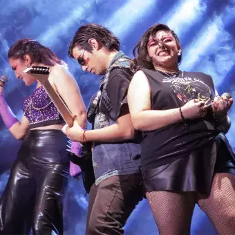 Alumno tocando la guitarra con una cantante a cada lado en poses rockeras como parte del Ensamble IMMORTALITY.