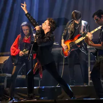 Cantante en pose de rock con tres guitarristas en el fondo.