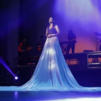 Chica cantante en el centro del escenario con una falda larga blanca sobre la cual se proyectan estrellas.  