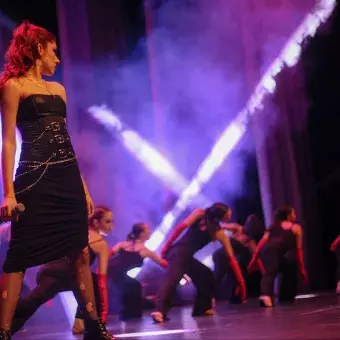 Cantante volteada hacia la izquierda con bailarinas de fondo. 