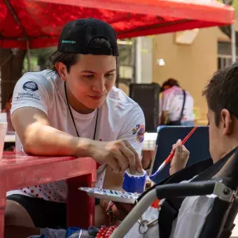 Estudiante ayudando a participante en su manualidad en Vive Extremo Camp