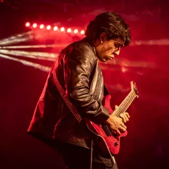 Andrés, guitarrista, en el escenario de Tec's Got Talent en el campus Hidalgo, concentrado en su interpretación con una guitarra eléctrica bajo luces rojas.