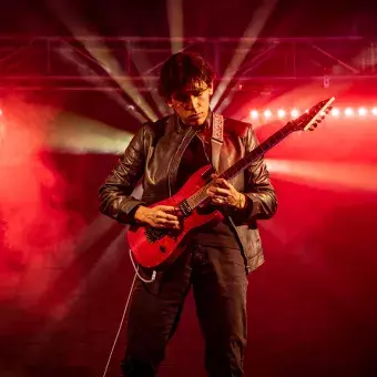 Andrés Ortega en un solo de guitarra, rodeado de luces rojas y un fondo de humo.