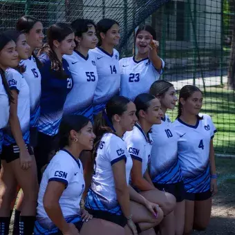 Alumnas posan para foto en equipo viendo fuera de cuadro mientras una de ellas apunta al frente hacia la cámara. 