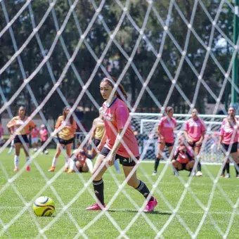 Vista de una jugadora de futbol a través de la red de la portería. 