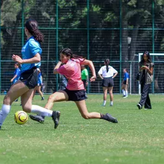 Jugadora de fútbol corre mientras patea el balon. 