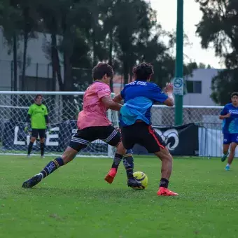 Jadores de fútbol compiten por el balón de espaldas a la cámara. 