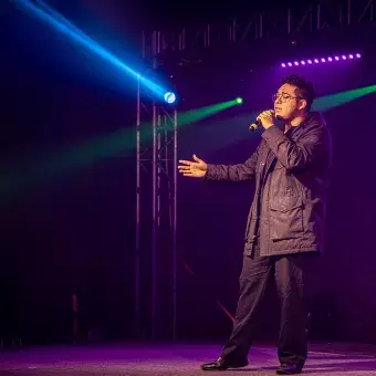 Eric González, estudiante de ingeniería y cantante, interpretando en el escenario. Con micrófono en mano y luces de colores que lo iluminan.