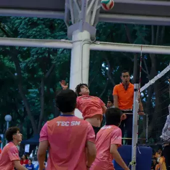 Jugador de voleibol saltando para rematar el balón mientras el otro equipo salta para bloquearlo. 