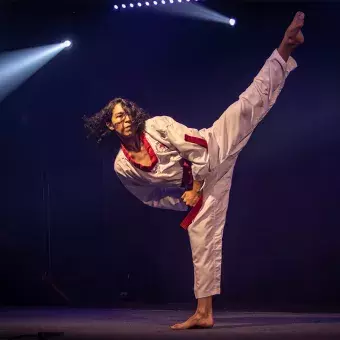 Rod Mendoza, karateka, ejecutando una patada alta con equilibrio durante su presentación en Tec's Got Talent en un escenario iluminado.