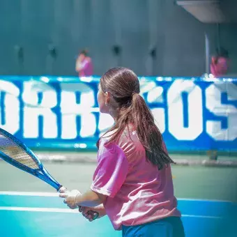 Alumna de espaldas sosteniendo raqueta de tenis. 