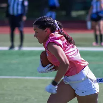 Chica corriendo con balon de futbol americano bajo el brazo. 