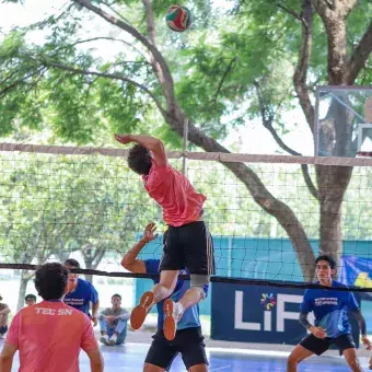 Jugador de voleibol saltando para rematar balon. 