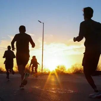 Personas corriendo a contraluz con amanecer de fondo