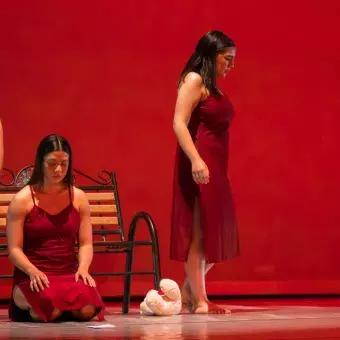 Tres bailarinas realizan formas sobre banco en un fondo rojo