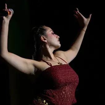 Mujer vestida de rojo sosteniendo ambos brazos en el aire en posición de belly dance. 